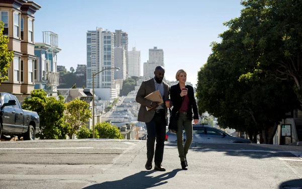 HD PC desktop wallpaper from TV show Murder in the First: two detectives stride up a sunlit San Francisco hill, skyline and row houses behind them.