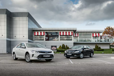 A white Toyota Camry and a black car parked side by side in front of a modern building, captured in a 4K Ultra HD desktop wallpaper.