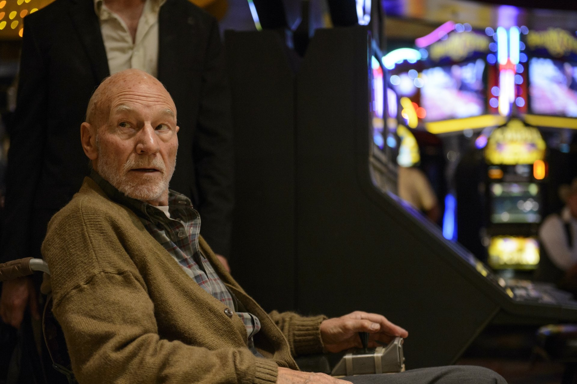HD desktop wallpaper featuring Patrick Stewart as Professor X in the movie Logan, sitting in a wheelchair with a concerned expression, with a background of vibrant slot machines.