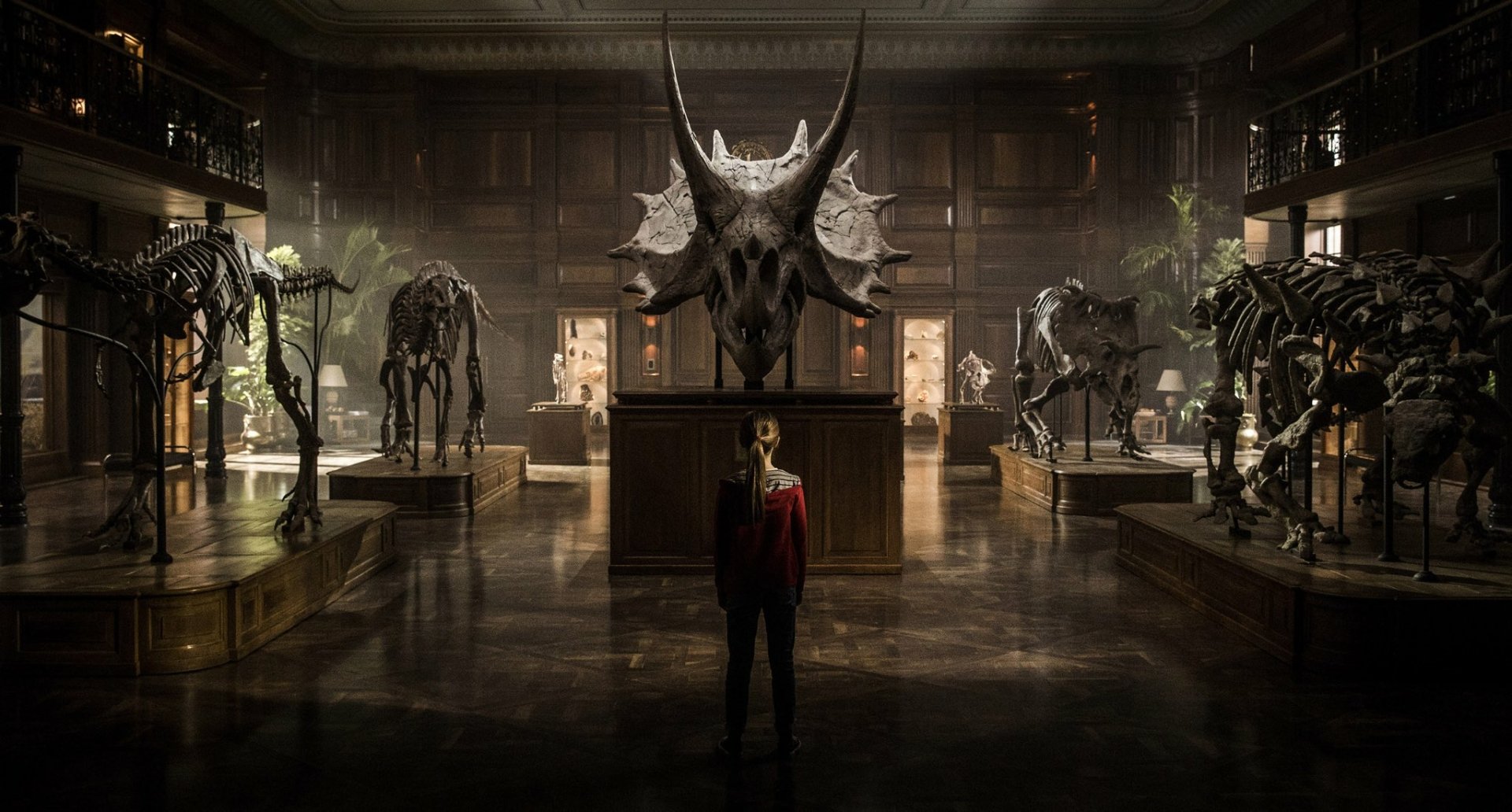 A scene from Jurassic World: Fallen Kingdom, featuring a character standing in an elegant room surrounded by dinosaur skeletons, creating a dramatic and captivating atmosphere.