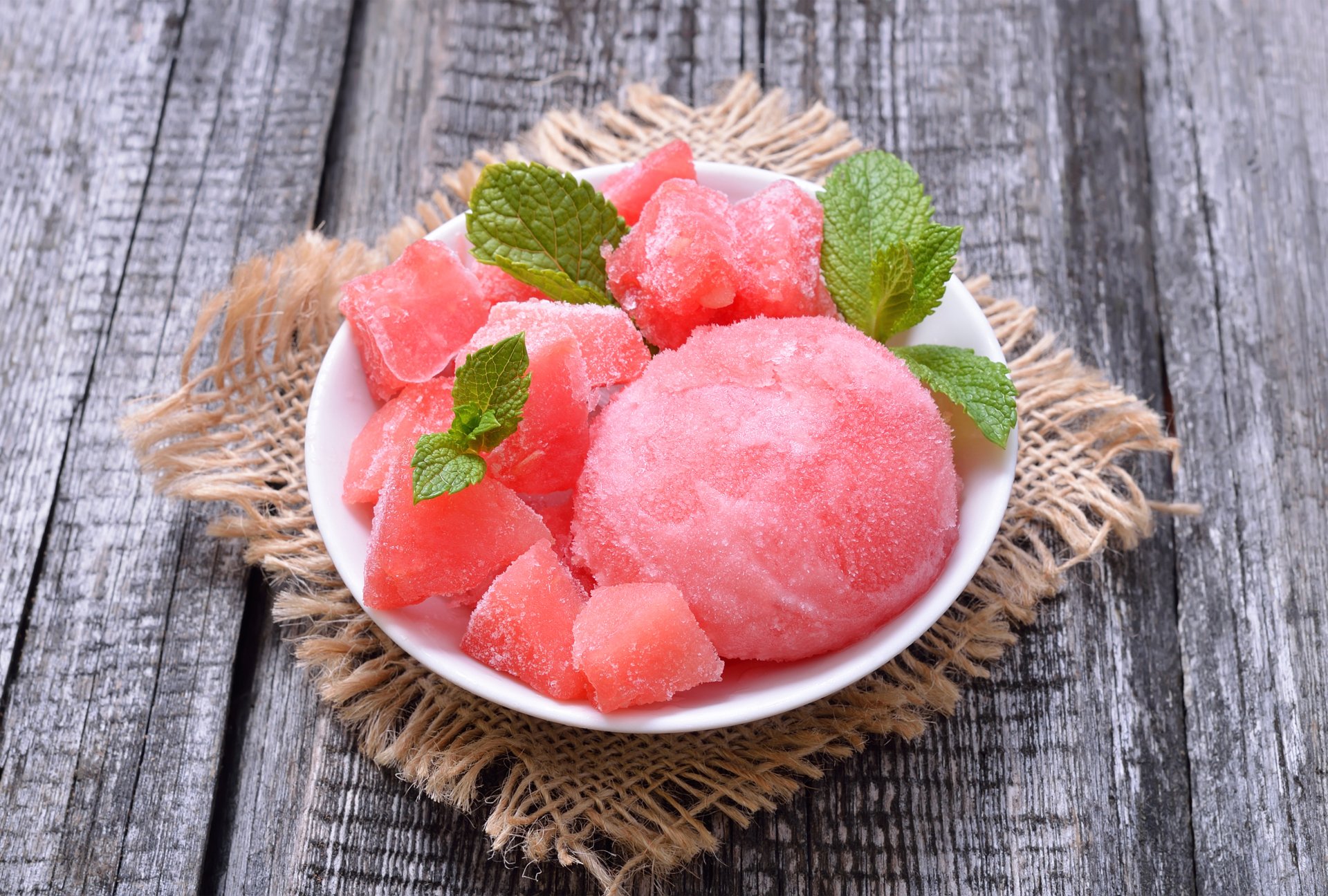 A vibrant close-up of pink ice cream and fruit cubes garnished with fresh mint leaves on a rustic wooden surface, captured in stunning 4K Ultra HD for PC desktop wallpaper.