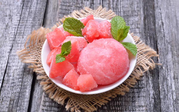 A vibrant close-up of pink ice cream and fruit cubes garnished with fresh mint leaves on a rustic wooden surface, captured in stunning 4K Ultra HD for PC desktop wallpaper.