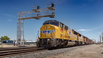 HD desktop wallpaper featuring a powerful freight train traveling on tracks under a clear blue sky, showcasing the dynamic motion of this vehicle.