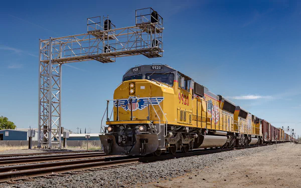 HD desktop wallpaper featuring a powerful freight train traveling on tracks under a clear blue sky, showcasing the dynamic motion of this vehicle.