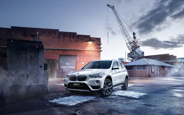 White BMW X1 SUV parked in an industrial area at dusk, captured in high definition for a PC desktop wallpaper and background.