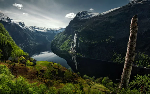 HD PC desktop wallpaper of nature: a fjord framed by towering mountains and trees, their forms mirrored in a calm river reflecting snowy peaks and green slopes.