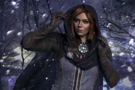 HD wallpaper featuring a cosplayer as Leliana from Dragon Age: Inquisition, standing in snow with a detailed costume and hooded cloak.