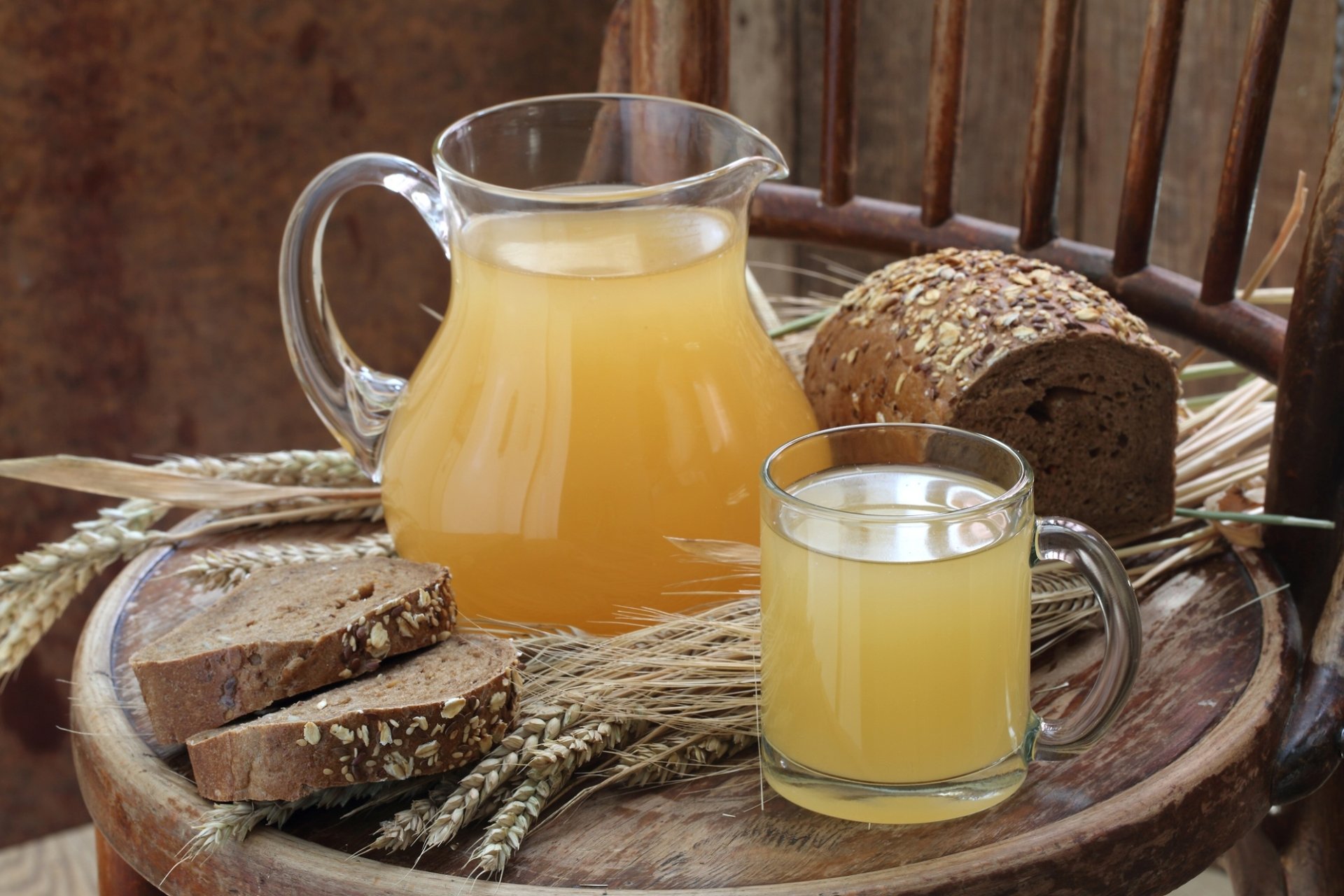 HD desktop wallpaper still life: pitcher and mug of golden juice, sliced whole-grain bread and wheat stalks on a rustic wooden board.