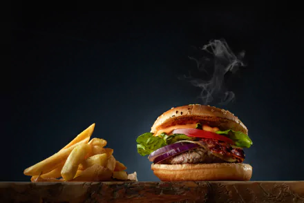 HD desktop wallpaper featuring a juicy burger with lettuce, tomato, and onions, alongside a serving of golden french fries, set against a dark background.