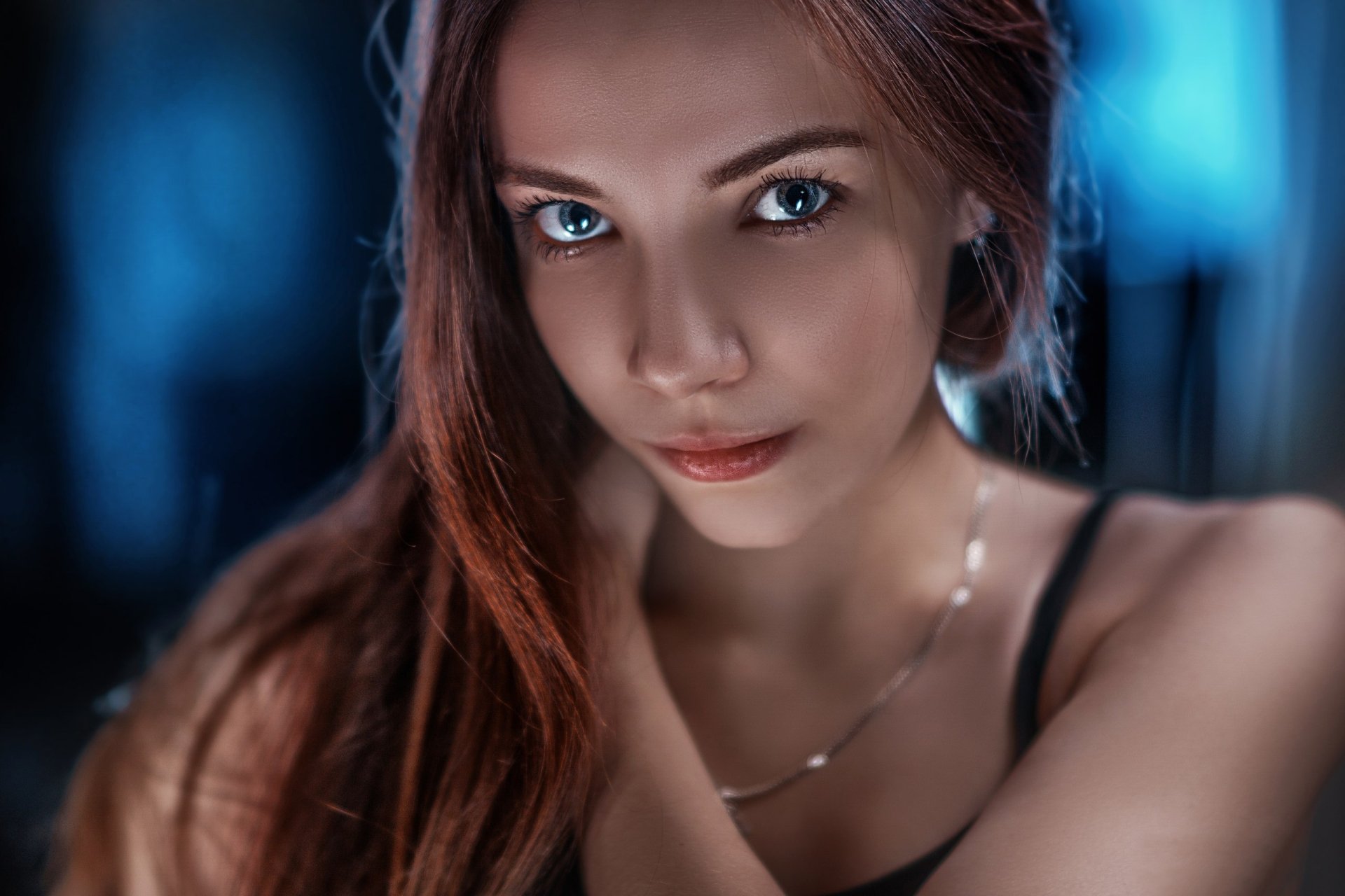 HD desktop wallpaper featuring a close-up of a redhead woman model with striking blue eyes and a softly lit face.