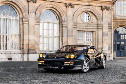 Black Ferrari Testarossa supercar parked on cobblestone in front of historic building, captured in high-definition for a striking PC desktop wallpaper.