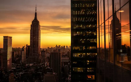 Sunset cityscape of New York featuring the Empire State Building and skyscraper reflections in a window, captured in an HD desktop wallpaper background.