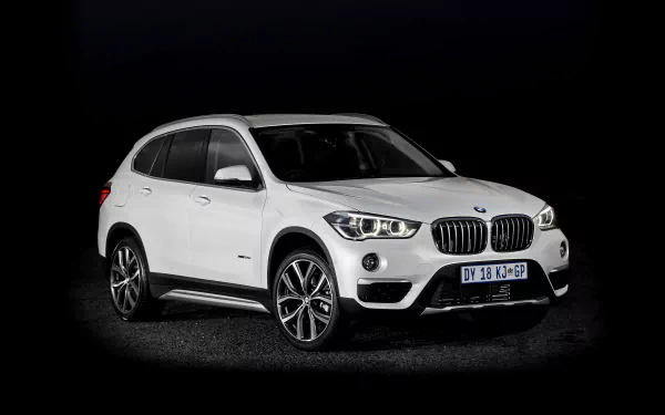 HD wallpaper of a sleek white BMW X1 SUV, front and side view, set against a dark background.