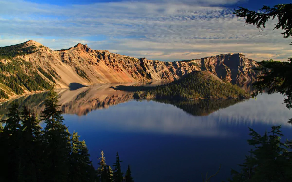 Crystal-clear reflection of forested island and rugged cliffs in the serene waters of Crater Lake, captured in a high-definition nature scene.