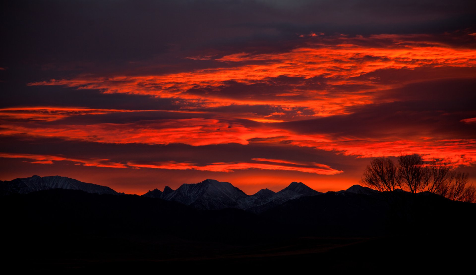 HD desktop wallpaper showcasing a stunning silhouette of mountains and trees against a dramatic orange sky at night, with clouds adding texture and depth to the mesmerizing nature scene.