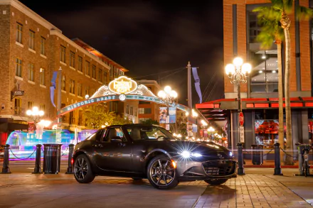 A sleek black Mazda MX-5 parked on a vibrant city street at night, captured in stunning 4K Ultra HD quality as a desktop wallpaper and background.