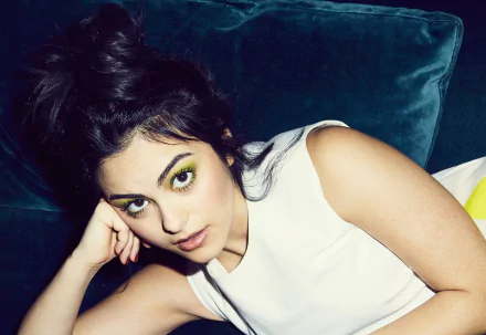 HD desktop wallpaper of Brazilian actress Camila Mendes with brunette hair and brown eyes, lying on a dark teal velvet surface, wearing a white sleeveless top.
