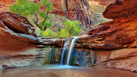 HD desktop wallpaper featuring a serene canyon landscape with a cascading waterfall and lush greenery against rugged red rock formations.