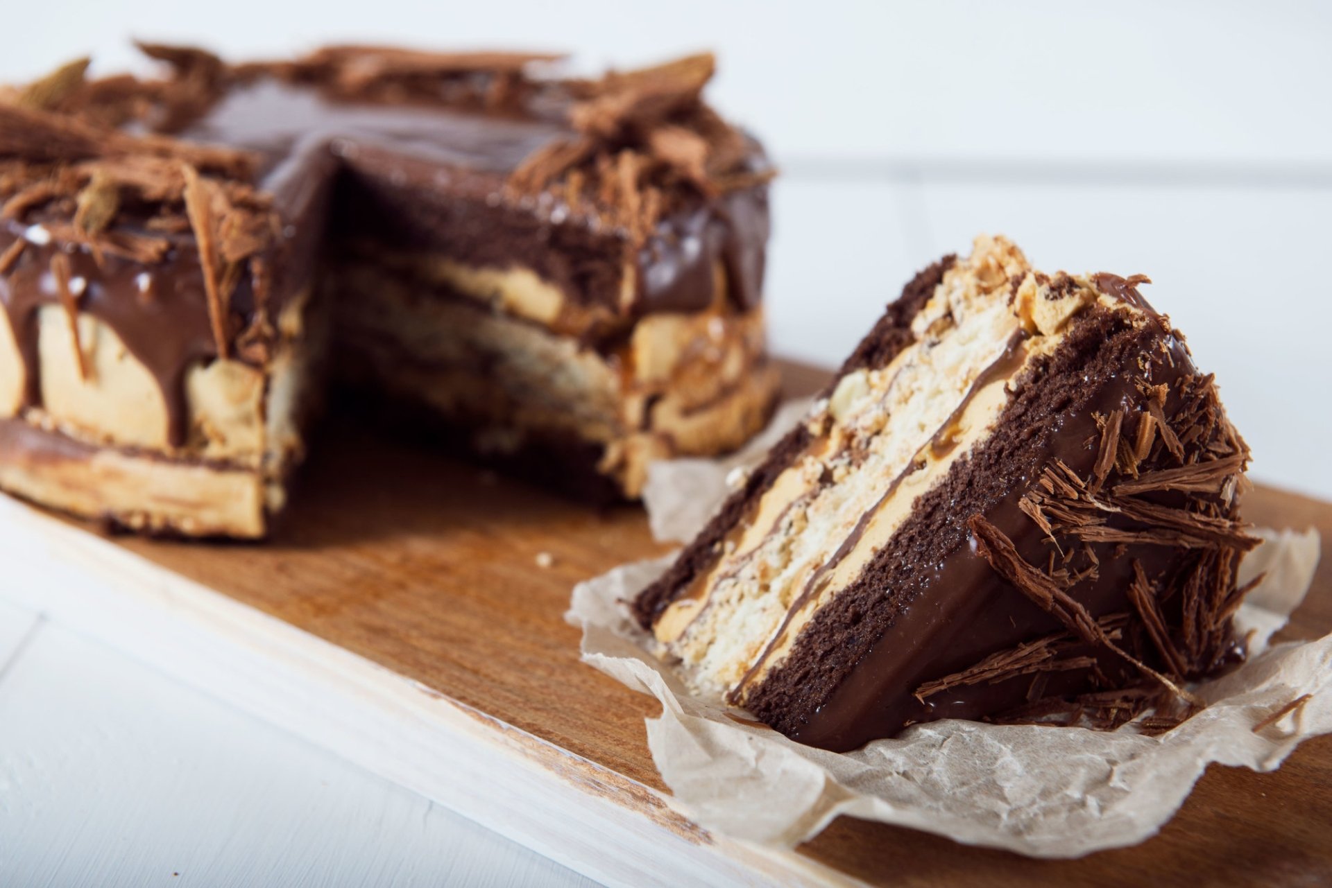 HD PC desktop wallpaper/background: close-up of a layered pastry cake — chocolate-coated slices with creamy filling and chocolate shavings on a wooden board, food photography.