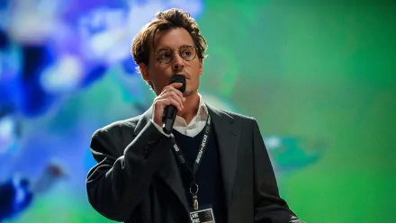 HD PC desktop wallpaper of an actor onstage speaking into a microphone, themed for the movie Transcendence, with a soft green-blue blurred background.