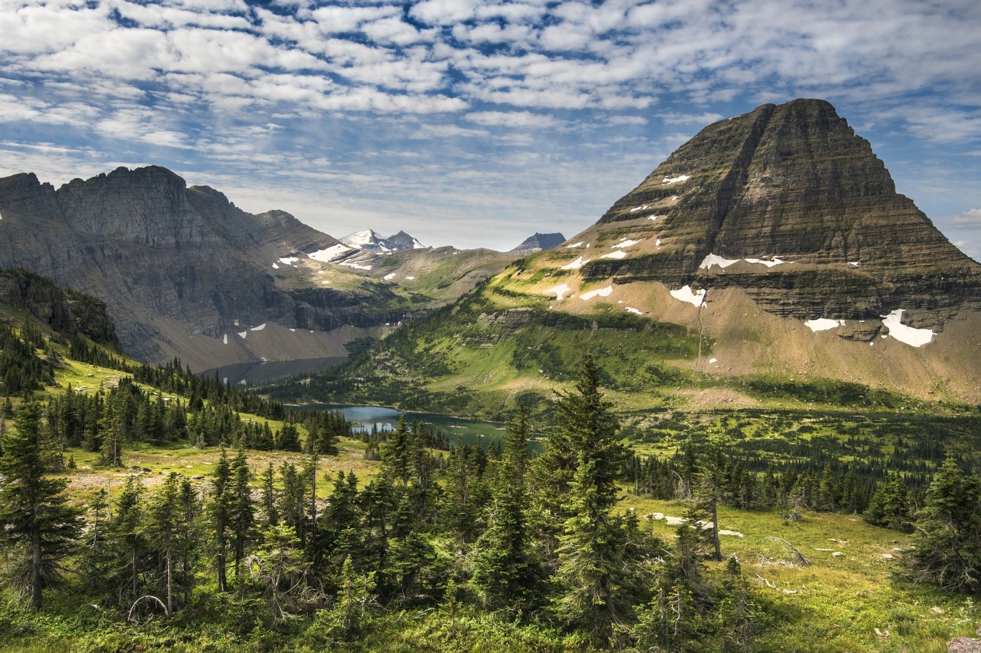 A stunning HD wallpaper of Glacier National Park in Montana, USA, showcasing a serene lake, lush wilderness, and rugged mountains under a partly cloudy sky, highlighting the natural beauty and landscape.