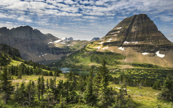 A stunning HD wallpaper of Glacier National Park in Montana, USA, showcasing a serene lake, lush wilderness, and rugged mountains under a partly cloudy sky, highlighting the natural beauty and landscape.