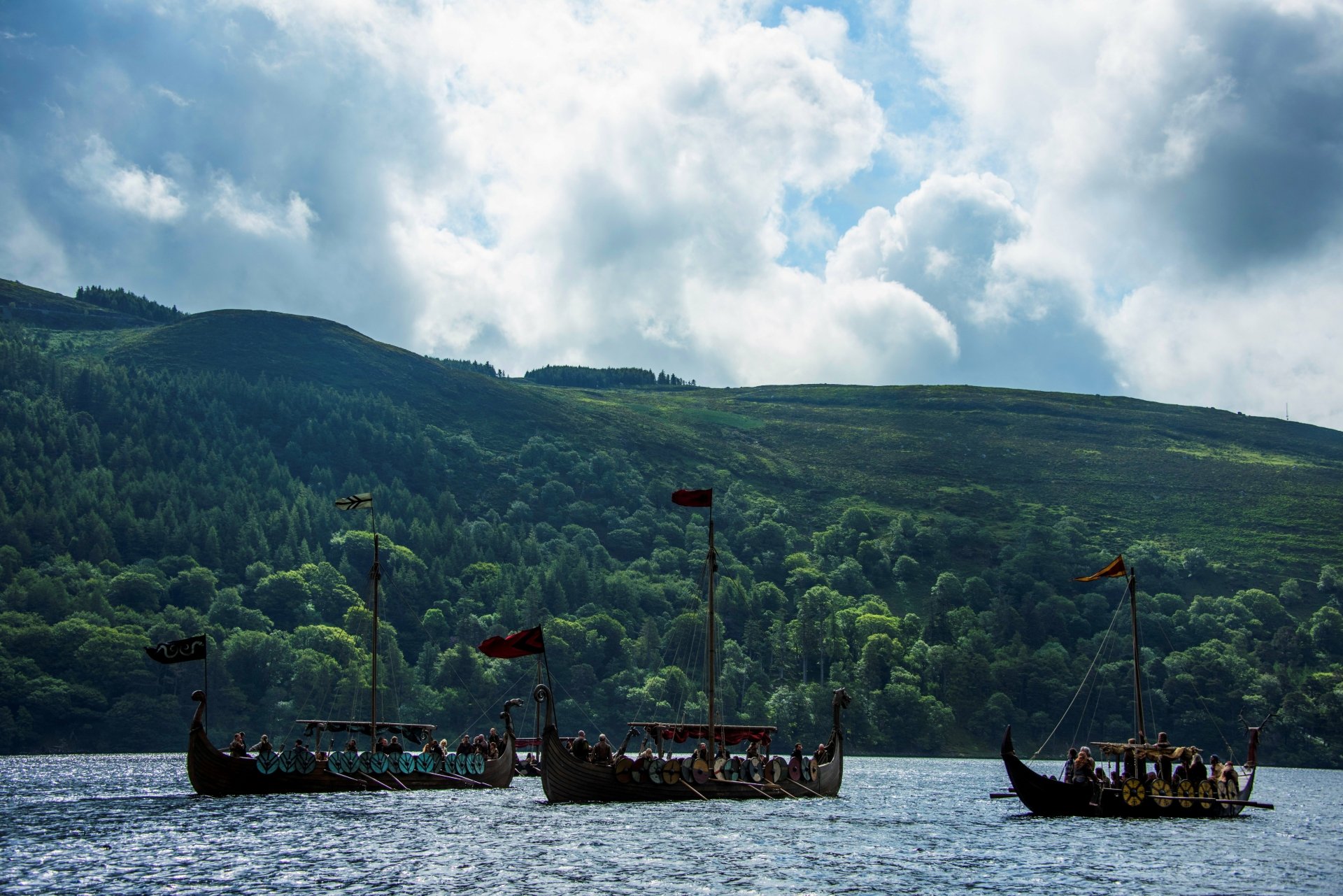 Vikings (2013) TV show 5K Ultra HD PC desktop wallpaper: silhouetted longships and crew rowing across a fjord with forested hills under dramatic clouds.