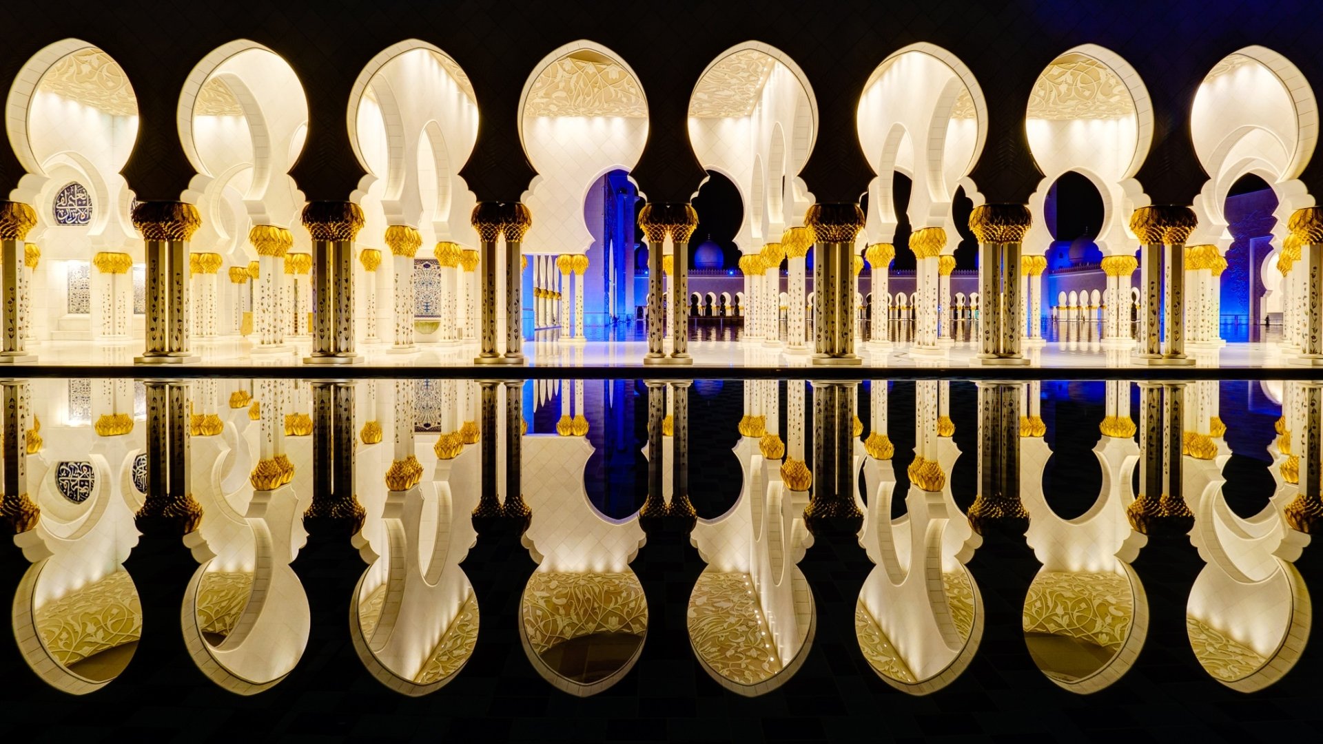 Sheikh Zayed Grand Mosque in Abu Dhabi at night, showcasing its intricate architecture and glowing arches reflected perfectly in still water.