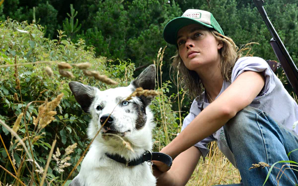 HD desktop wallpaper featuring Margot Robbie from the movie Z for Zachariah, sitting outdoors with a dog against a lush green background.