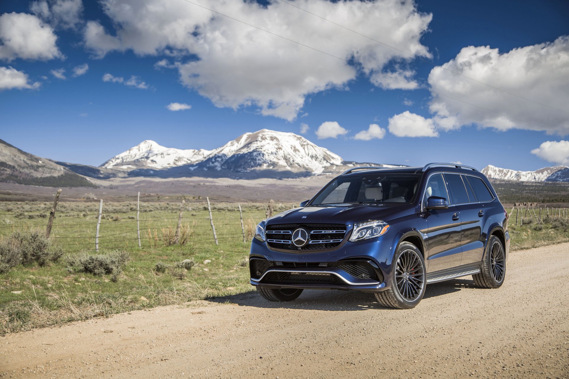 A black Mercedes-Benz GL-Class SUV parked on a dirt road with snow-capped mountains and a blue sky in the background, presented as a 4K Ultra HD desktop wallpaper.