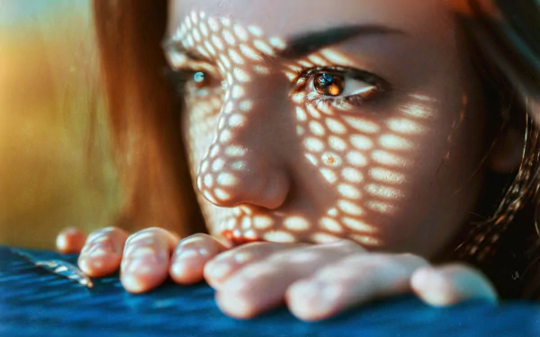Close-up of a woman's face with brown eyes, patterned light across her skin and fingers; HD PC desktop wallpaper and background.
