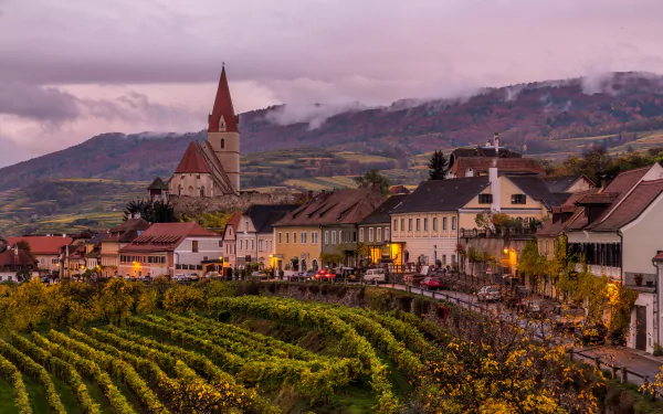 Scenic 4K Ultra HD view of an Austrian town featuring a church, houses, and vineyards set against a mountainous backdrop.