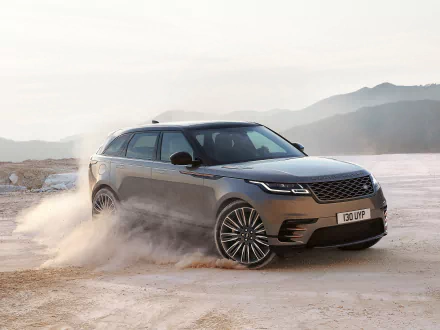 HD desktop wallpaper featuring a silver Range Rover SUV, captured mid-action on a sandy terrain with a mountainous background. The Land Rover vehicle exudes power and elegance.