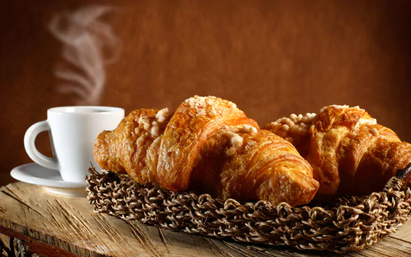 5K Ultra HD PC desktop wallpaper/background of breakfast food: golden croissant and steaming cup of coffee on a rustic wooden board.