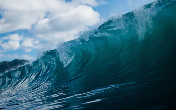 A powerful ocean wave curls under a partly cloudy sky, captured in vibrant detail as a 4K Ultra HD nature wallpaper and background.