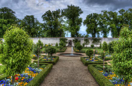 HD wallpaper of a beautiful, man-made garden in Germany during spring. The image features a central fountain, vibrant flowers, green bushes, and trees creating a picturesque backdrop.