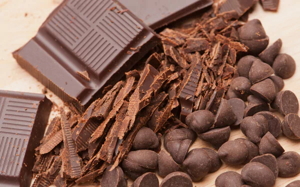 Close-up of chocolate bars, shavings, and chips in an 8K Ultra HD PC desktop wallpaper showcasing rich sweets and food textures.