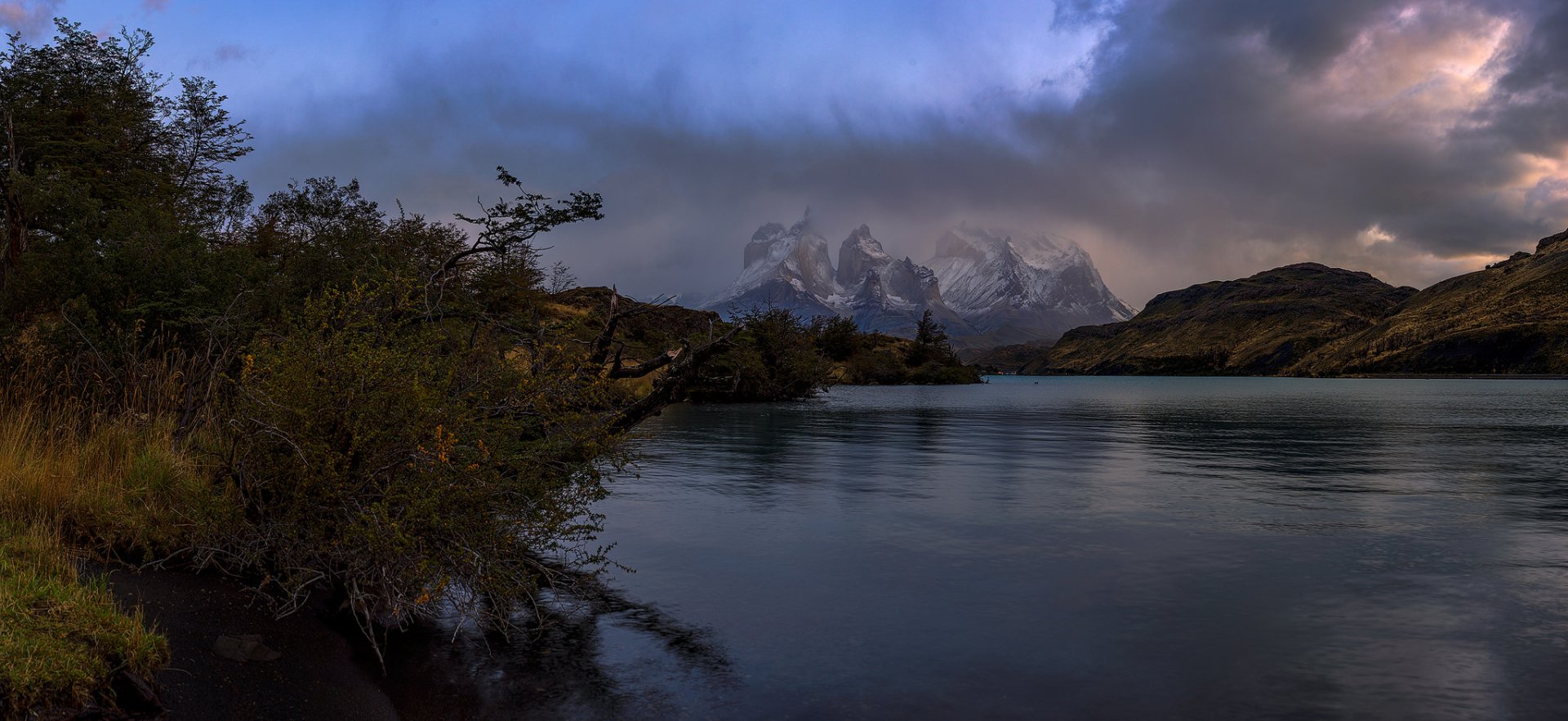 Fog envelops the rugged mountains of Torres del Paine in Chile’s Patagonia, reflected in the calm waters of this serene landscape from Torres del Paine National Park.