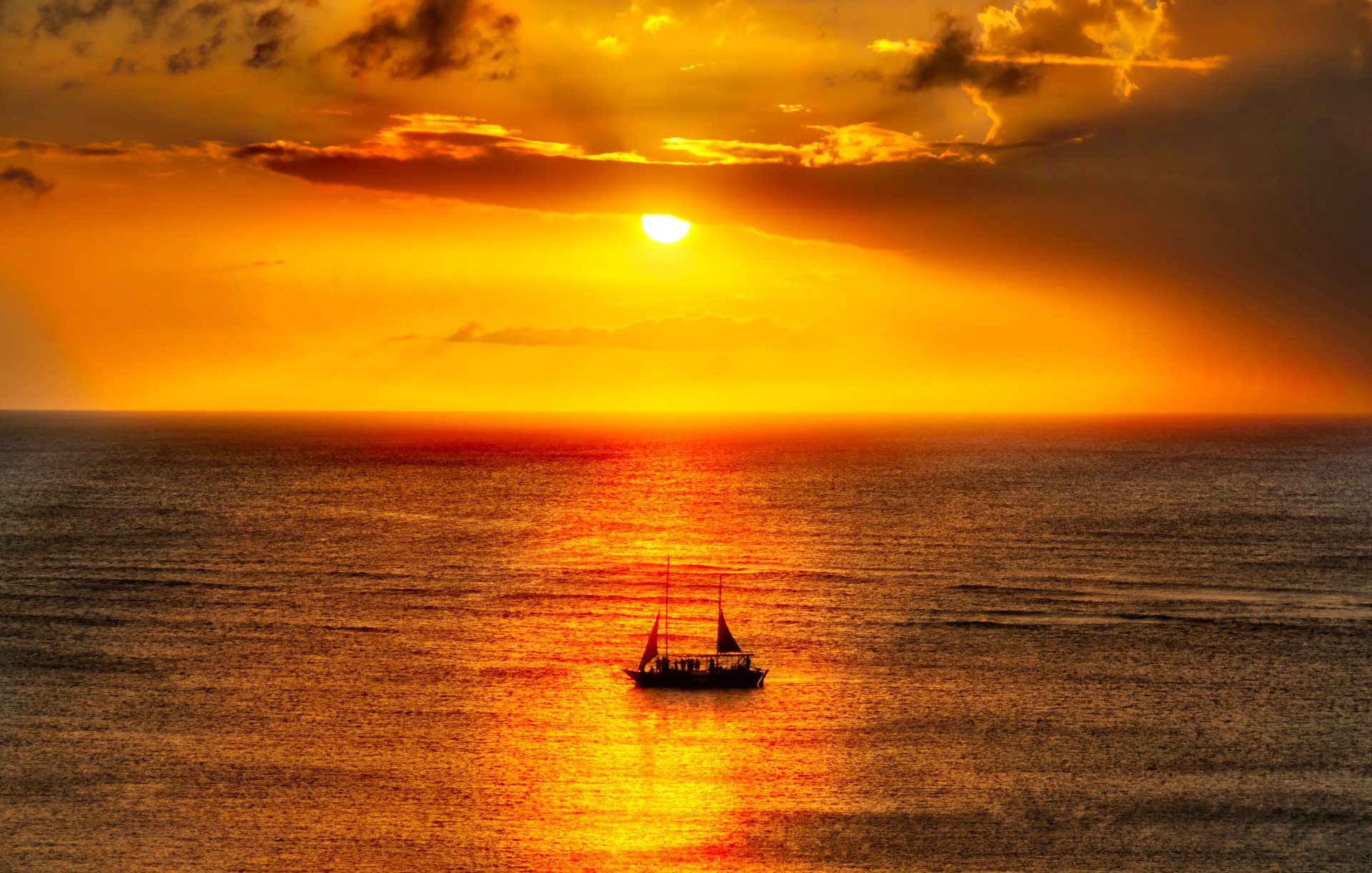 A breathtaking Caribbean seascape at sunset captured in HDR, featuring a sailboat on the horizon. This HD desktop wallpaper showcases the serene ocean and vibrant colors of the sunset.