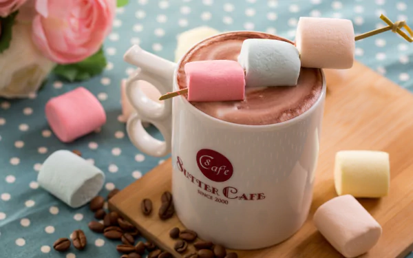 HD desktop wallpaper featuring a still life of a cup of hot chocolate topped with pastel marshmallows, surrounded by scattered marshmallows and coffee beans on a polka dot surface.
