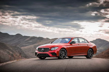 A high-definition desktop wallpaper of a sleek red Mercedes-Benz E-Class car set against a scenic mountain backdrop under a cloudy sky.