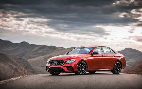 A high-definition desktop wallpaper of a sleek red Mercedes-Benz E-Class car set against a scenic mountain backdrop under a cloudy sky.