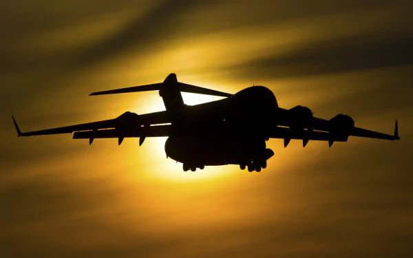Silhouette of a military warplane, the Boeing C-17 Globemaster III transport aircraft, backlit by a golden sun — 4K Ultra HD PC desktop wallpaper and background.