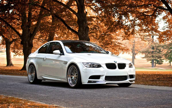 HD desktop wallpaper of a white BMW M3 coupé parked on a road lined with autumn trees, capturing the sleek design and vibrant foliage in the background.
