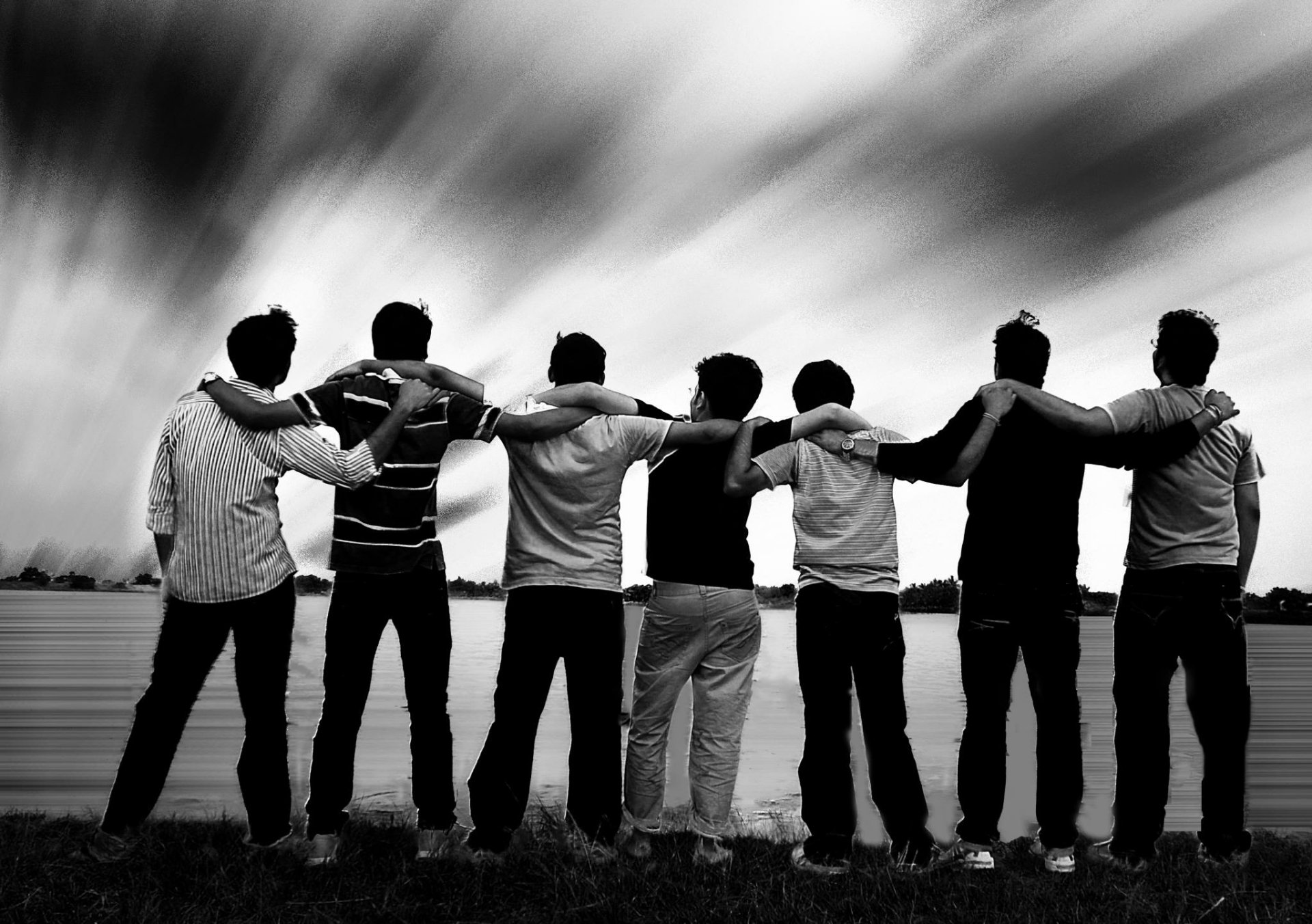 HD desktop wallpaper featuring a group of friends standing side by side with arms around each other, in black and white against a dramatic sky.