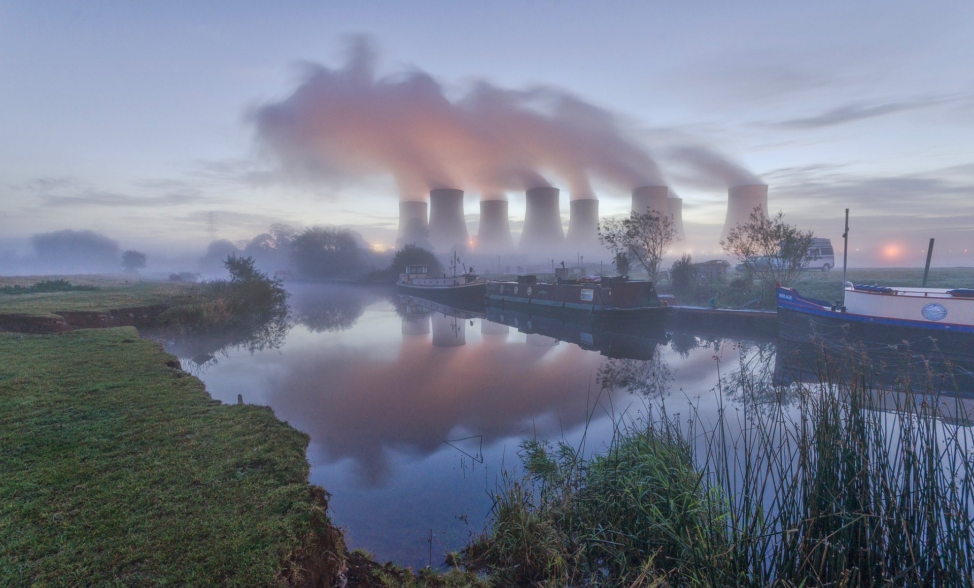 HD desktop wallpaper of a nuclear power plant with smoke rising from cooling towers, reflected in a calm river.