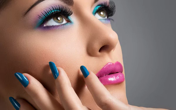 HD desktop wallpaper of a woman showcasing vibrant makeup, including turquoise nail polish, pink lipstick, and colorful eye shadow. Her face is prominently featured with a gray background.