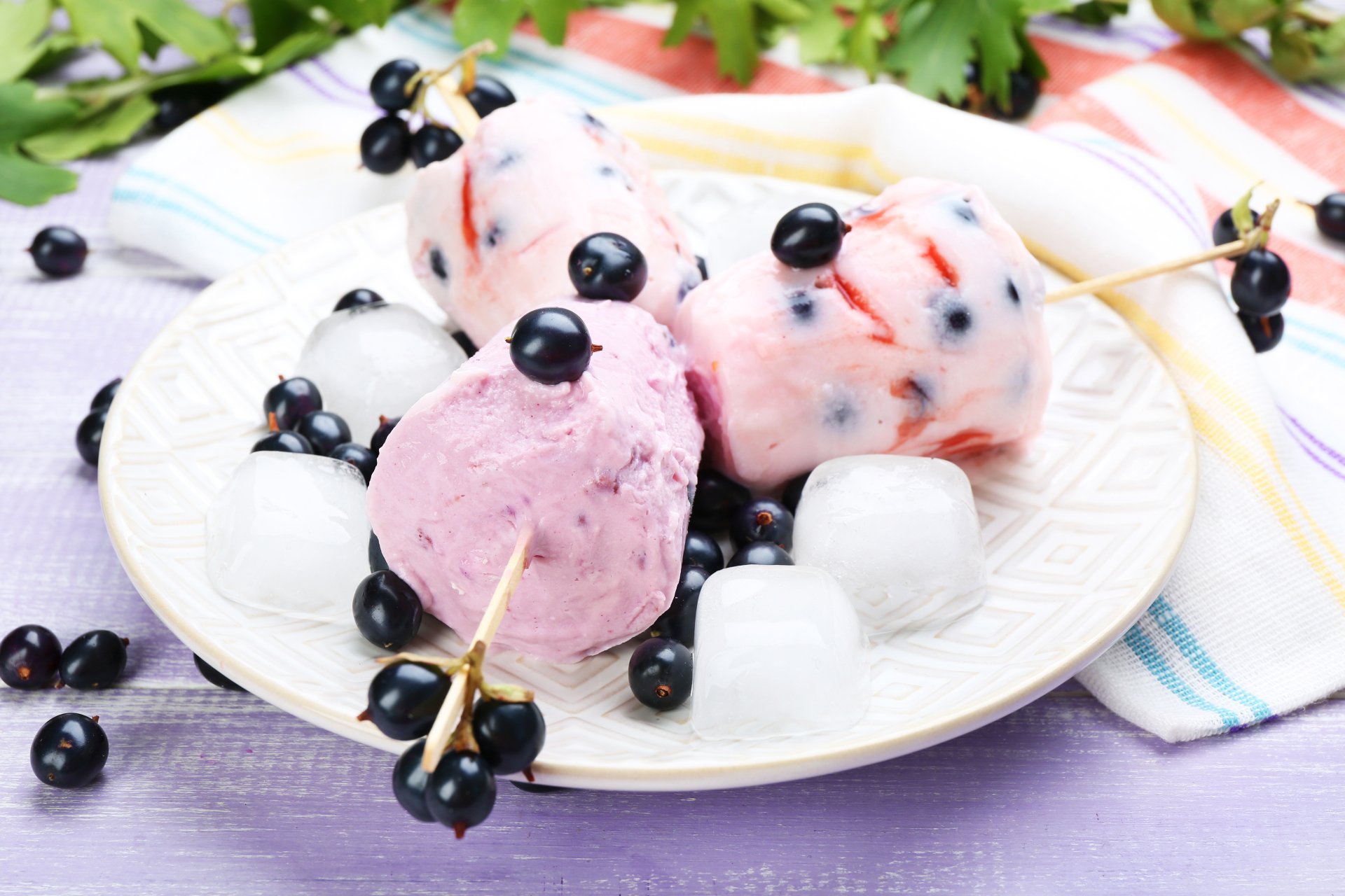 A 4K Ultra HD wallpaper featuring creamy berry ice cream bites served with ice cubes and fresh black currants on a white plate, showcasing sweet, refreshing food.