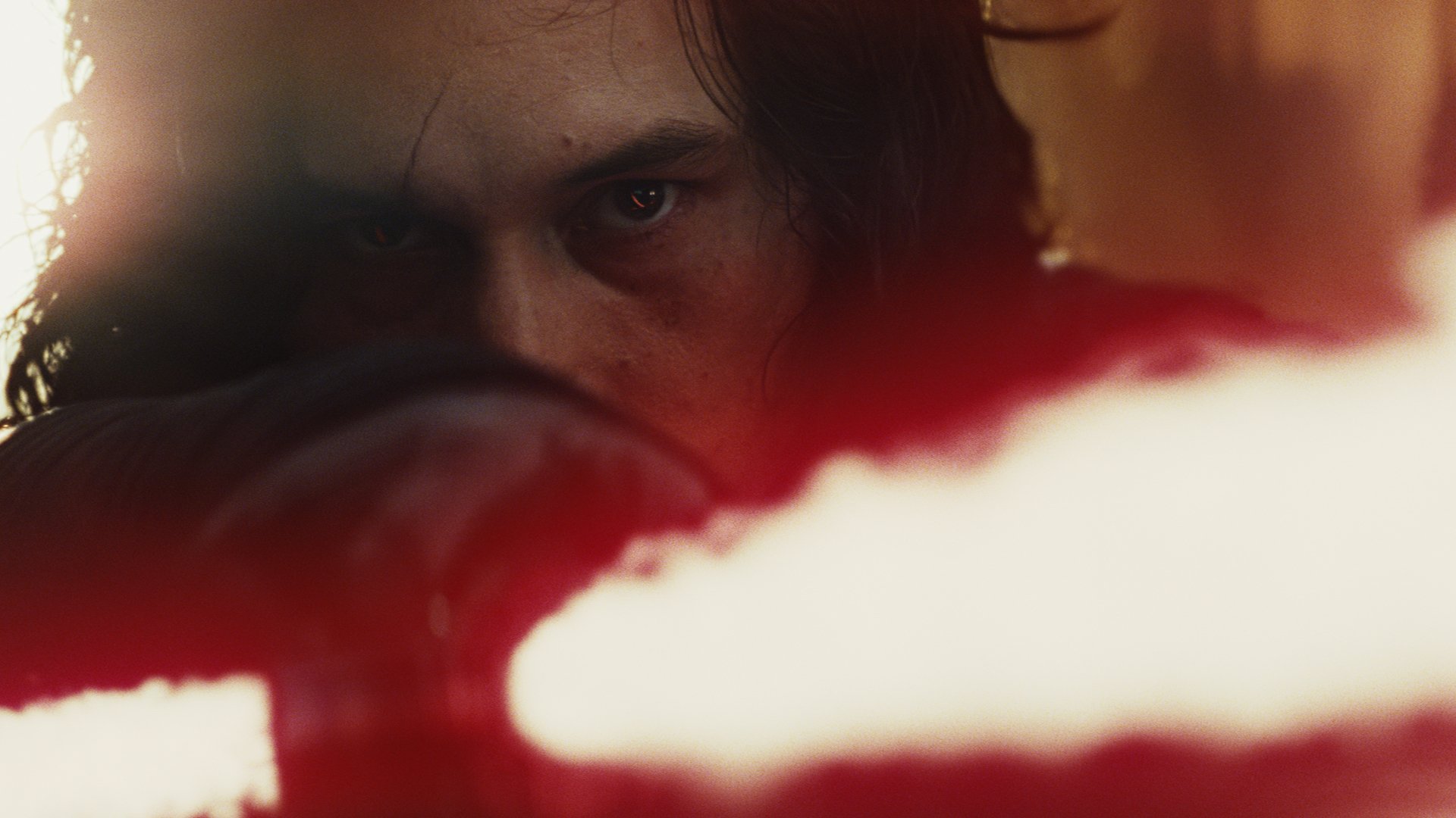 Close-up of a hooded, brooding figure igniting a red crossguard lightsaber in a cinematic scene from Star Wars: The Last Jedi — HD desktop wallpaper.