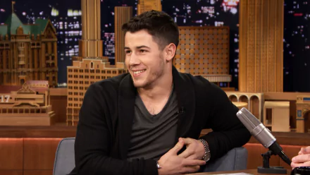 HD desktop wallpaper and background featuring a smiling man sitting in a talk show setting with city lights behind him.